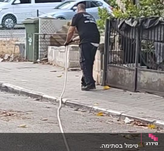 אדם מחזיק צינור על מדרכה ליד כביש